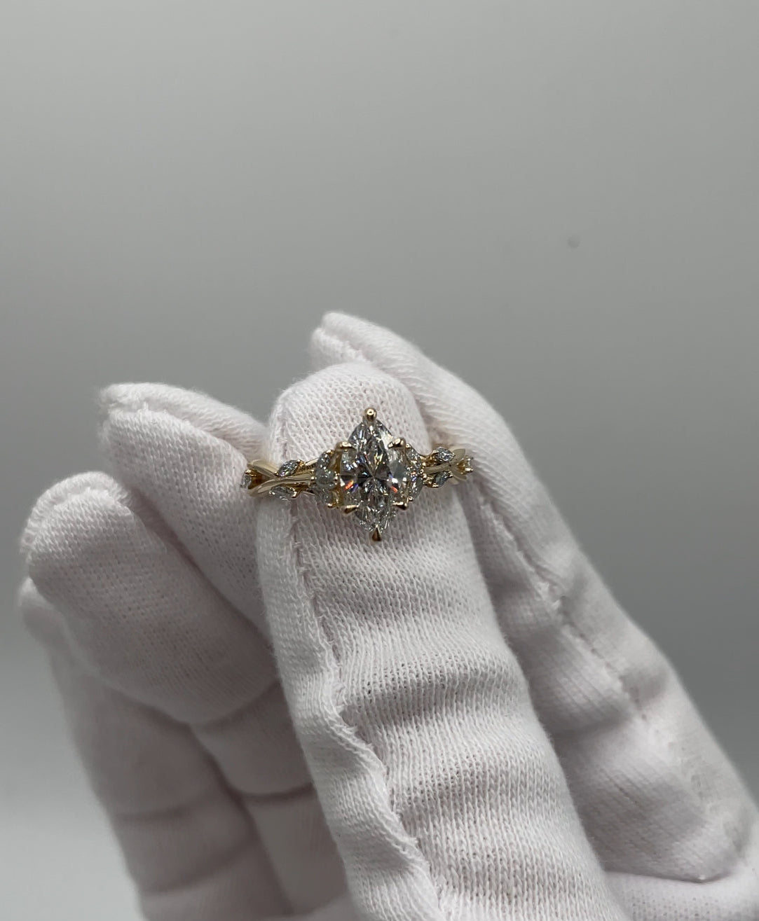 Golden Ivy ring with a diamond held by a gloved hand against a neutral background
