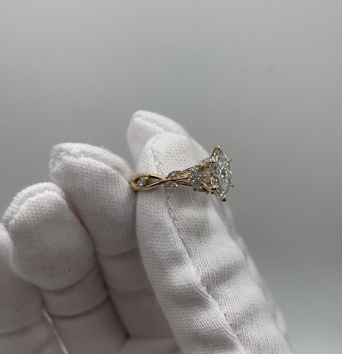Golden Ivy ring with Marquise diamond held by a gloved hand against a neutral background